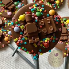 A round milk chocolate lollipop topped with a chocolate Lego man, chocolate Lego brick , colourful sprinkles and nestle mini smarties.